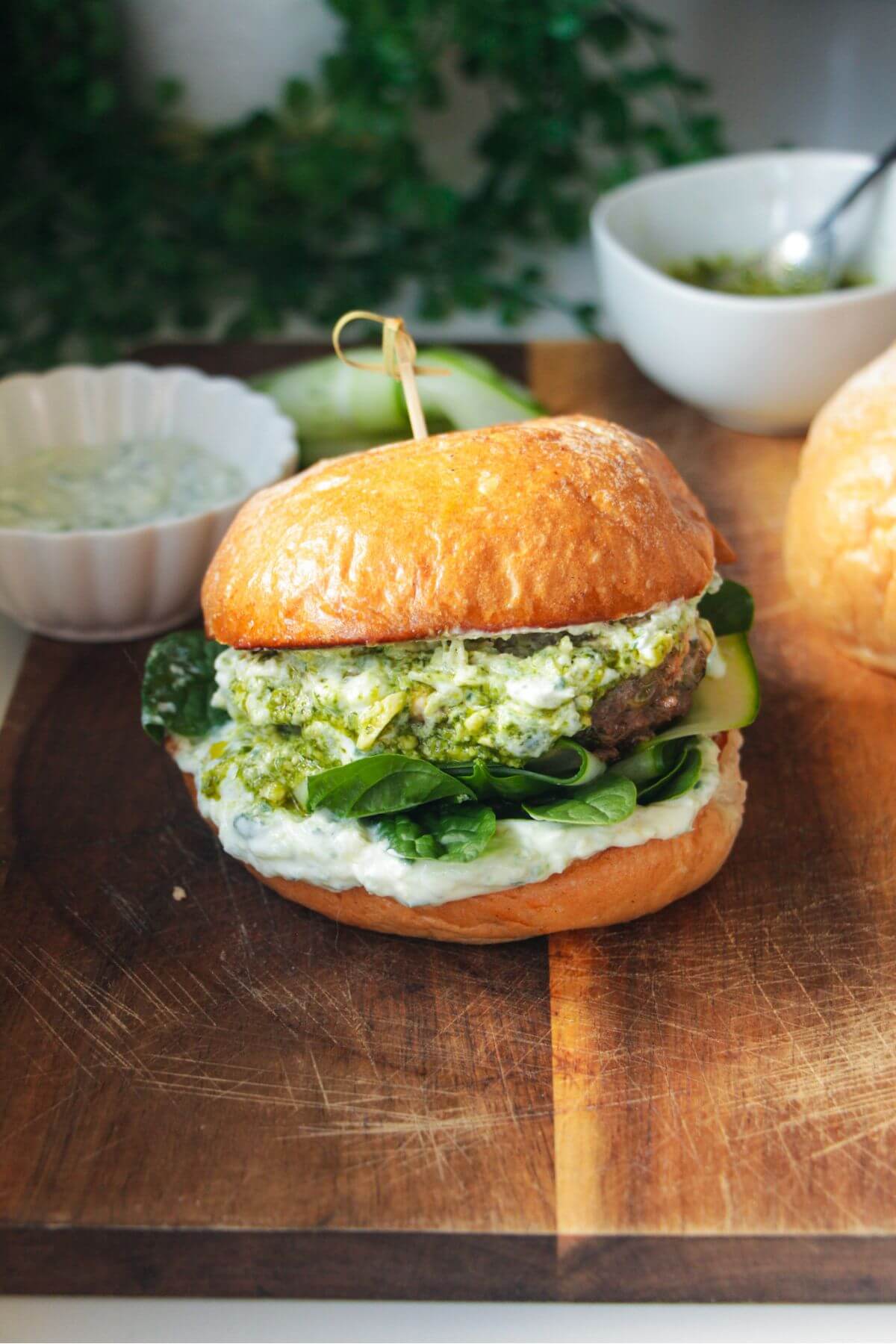 Lamb burger on a wooden board, with tzatziki and spinach.