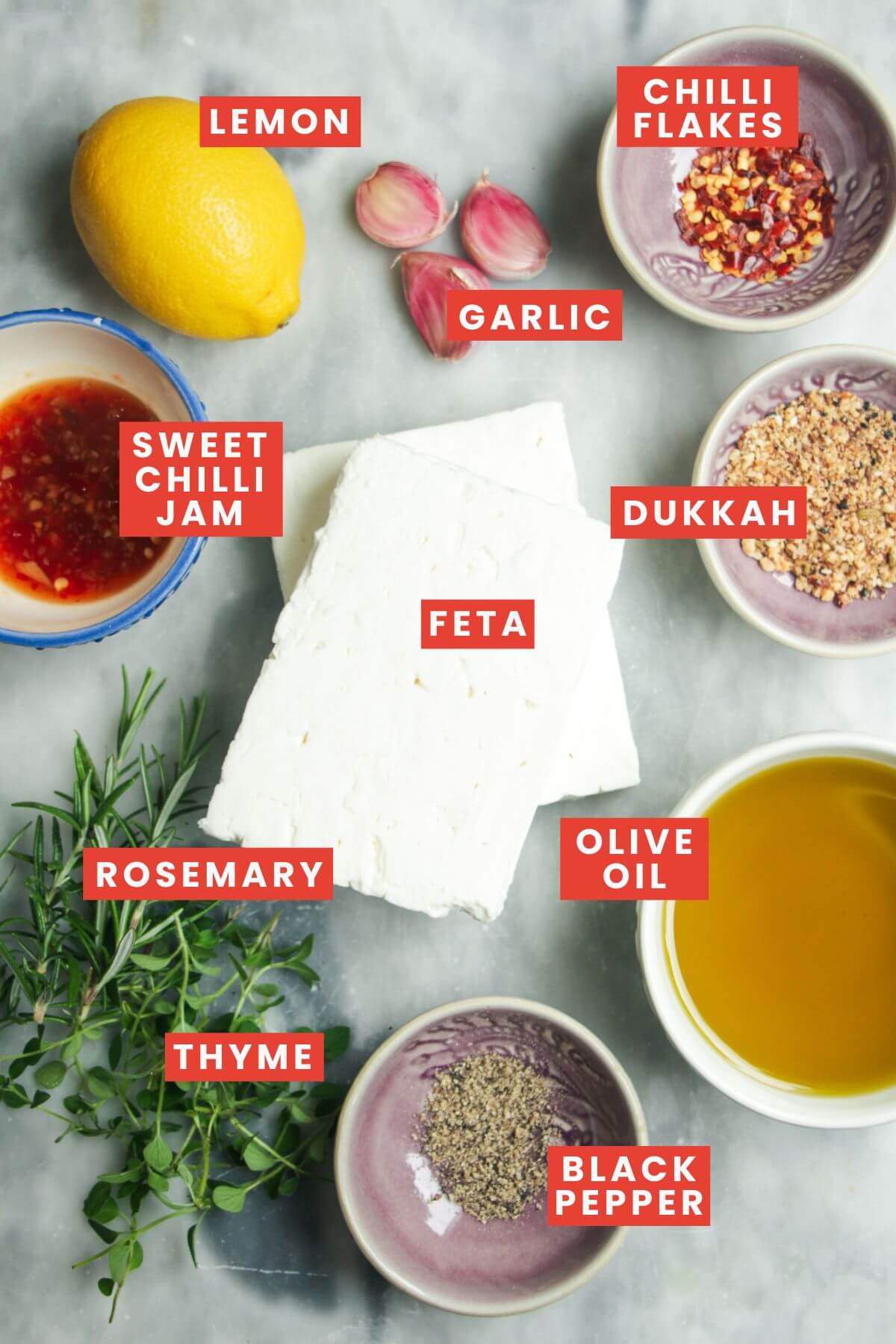 Ingredients for marinated feta laid out on a grey marble background.