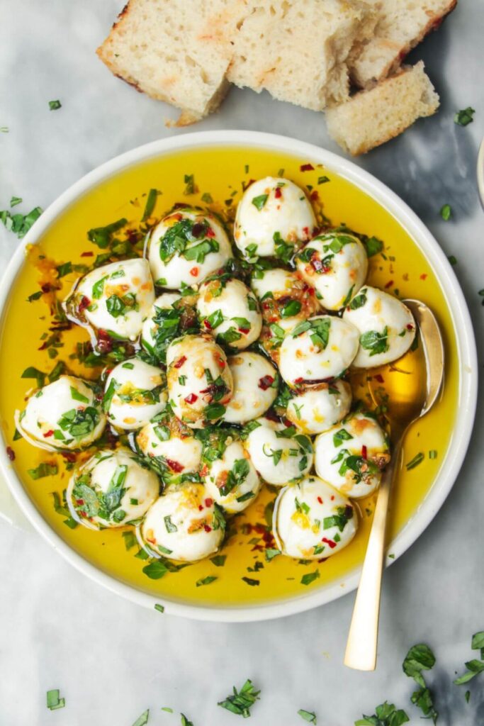 Marinated mini mozzarella balls in a small white plate with a gold spoon.