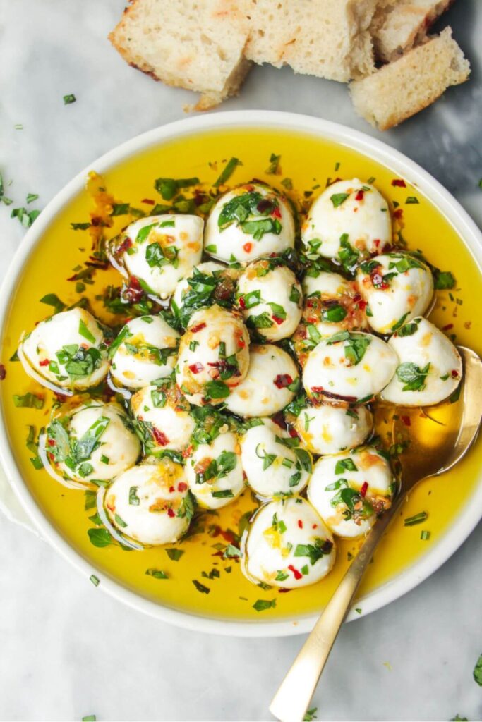 Marinated mini mozzarella balls in a small white plate with a gold spoon.