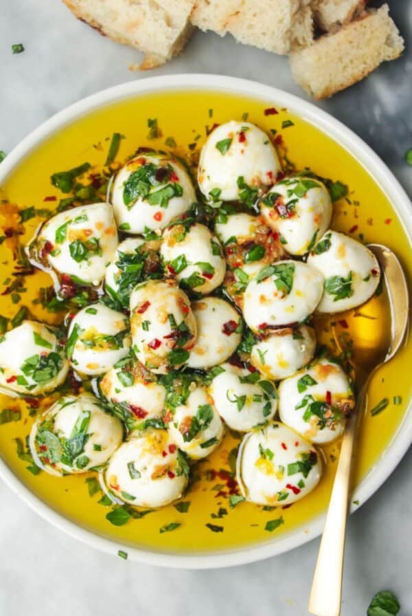 Marinated mini mozzarella balls in a small white plate with a gold spoon.