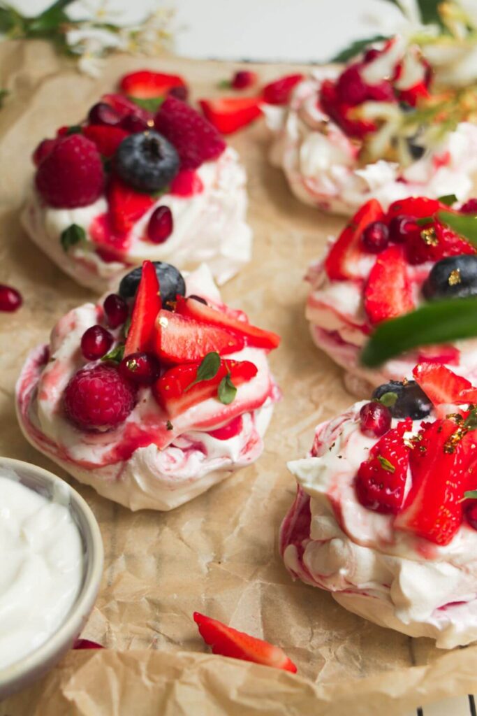 Close up of berry topped mini pavlovas on baking paper.