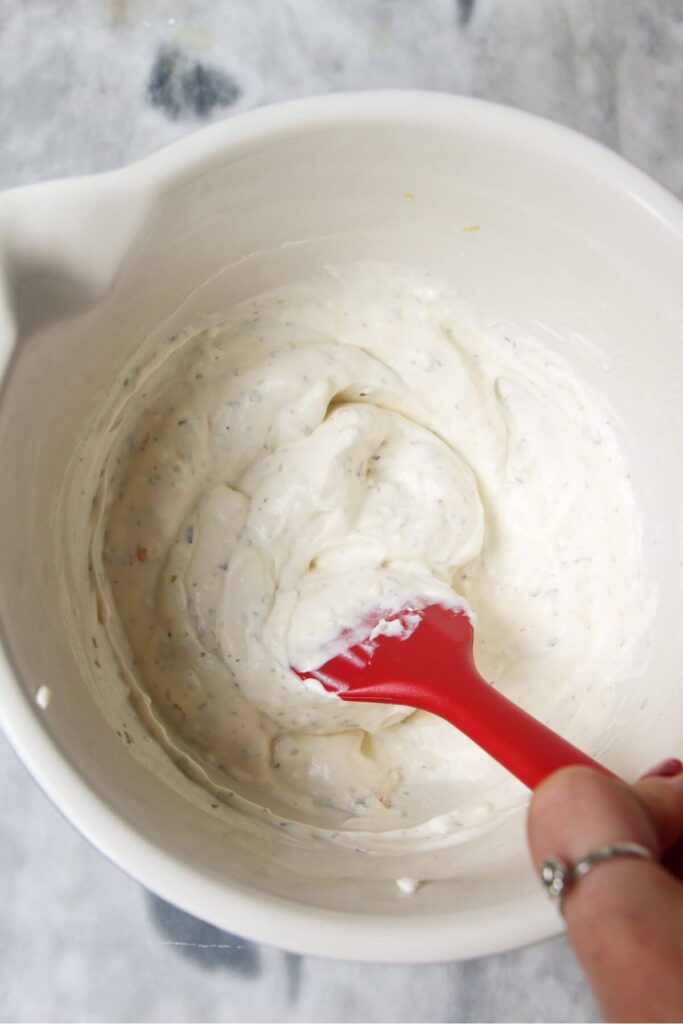 Red spatula stirring cream cheese mix in a white bowl.