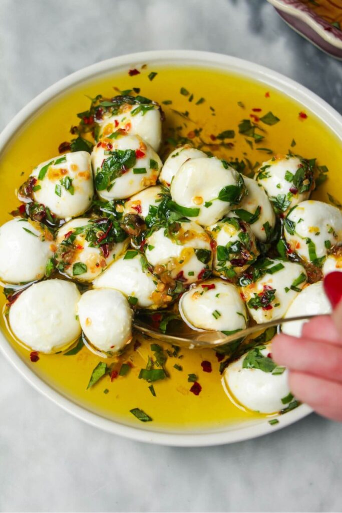 Mixing mozzarella balls through marinade in a small white plate.