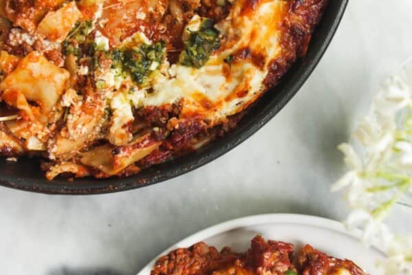 One pot lasagna served up on a small white plate, with pan of lasagna in the background.