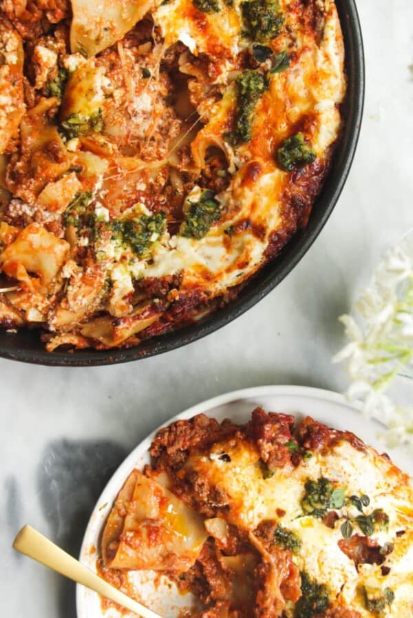 One pot lasagna served up on a small white plate, with pan of lasagna in the background.
