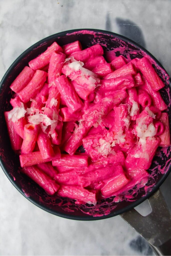 Grated parmesan on top of bright pink pasta in a small black pan.