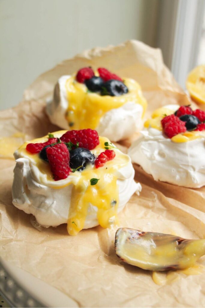 Close up of passionfruit and lemon curd topped pavlovas with berries on top.