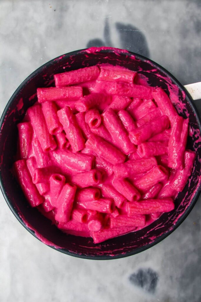 Bright pink pasta mixed in a small black pan.