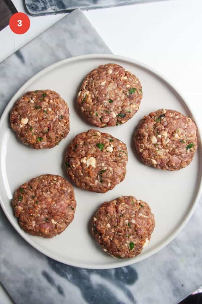 Six lamb burger patties on a large plate.