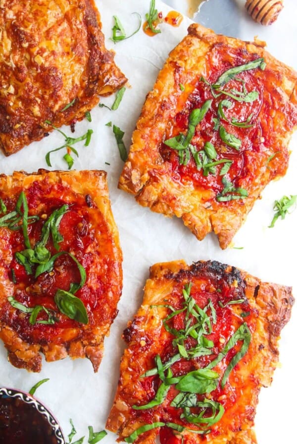 4 upside down puff pastry pizza tarts on baking paper, with a small bowl of chilli jam on the side.