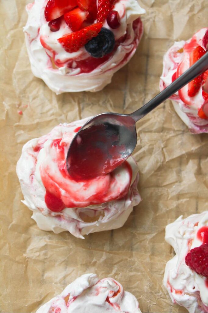 Spooning berry puree onto mini pavlova on a lined baking tray.
