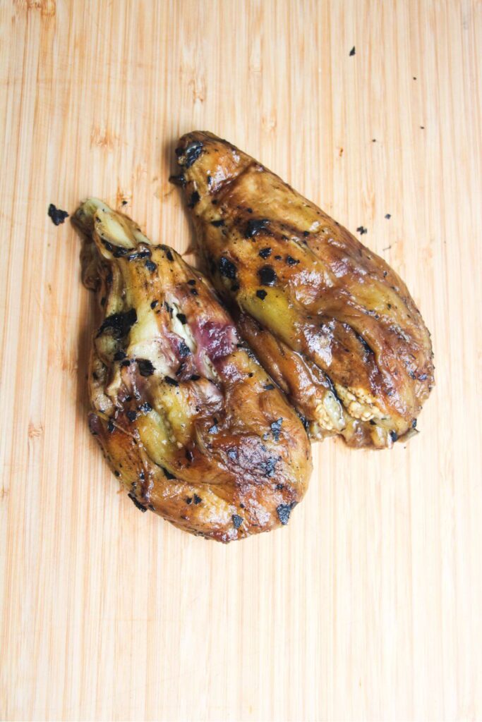 Two charred eggplants with their skins removed, on a wooden board.