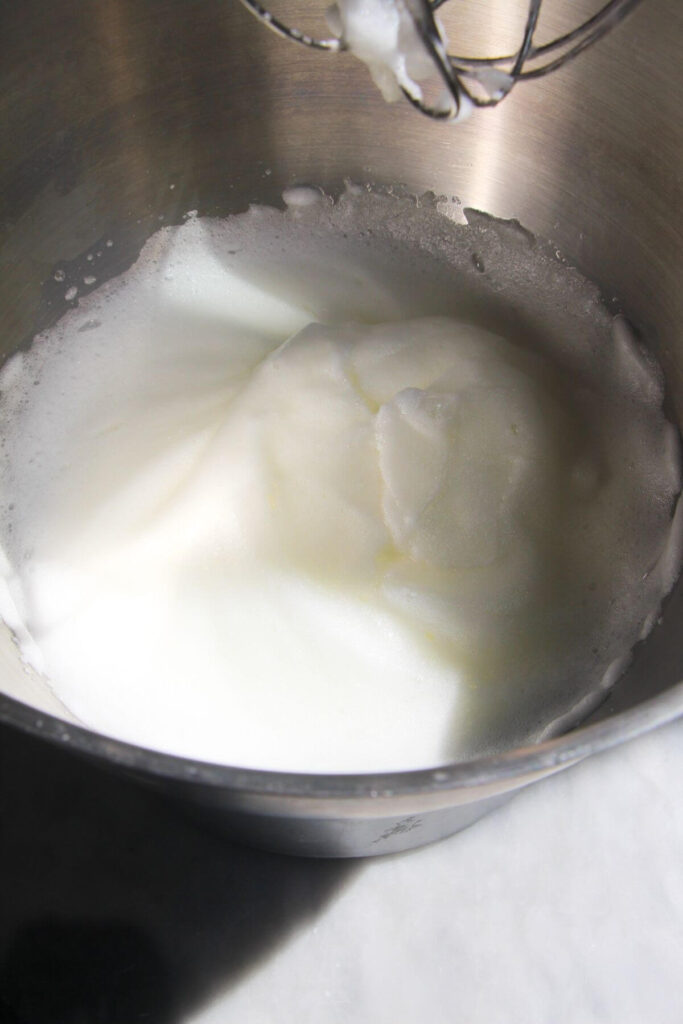 Egg whites whipped to soft peaks in a large silver bowl.