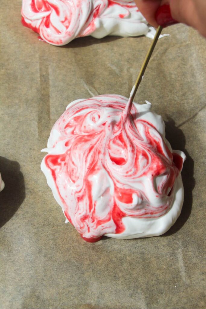Raspberry puree being swirled through meringue on baking paper lined tray with a skewer.