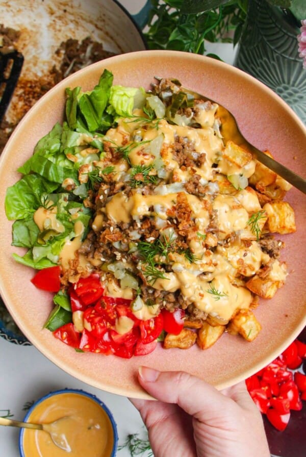 Holding loaded cheeseburger bowls drizzled with burger sauce.