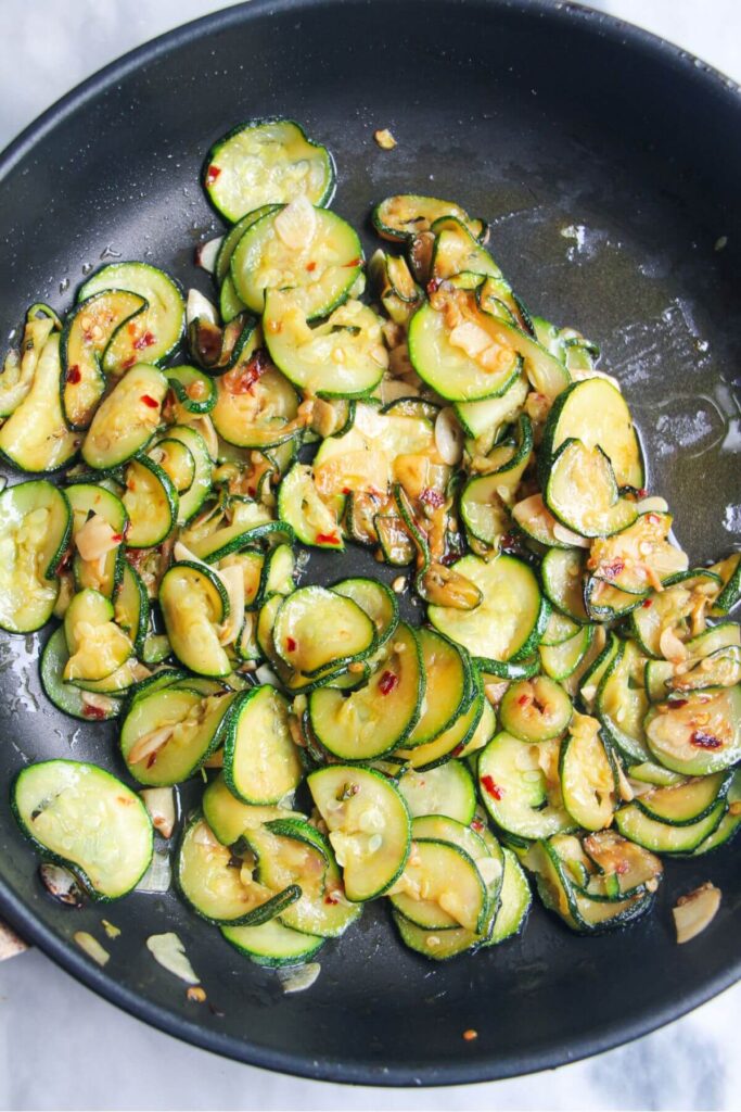Soft, cooked courgettes in a small black pan.