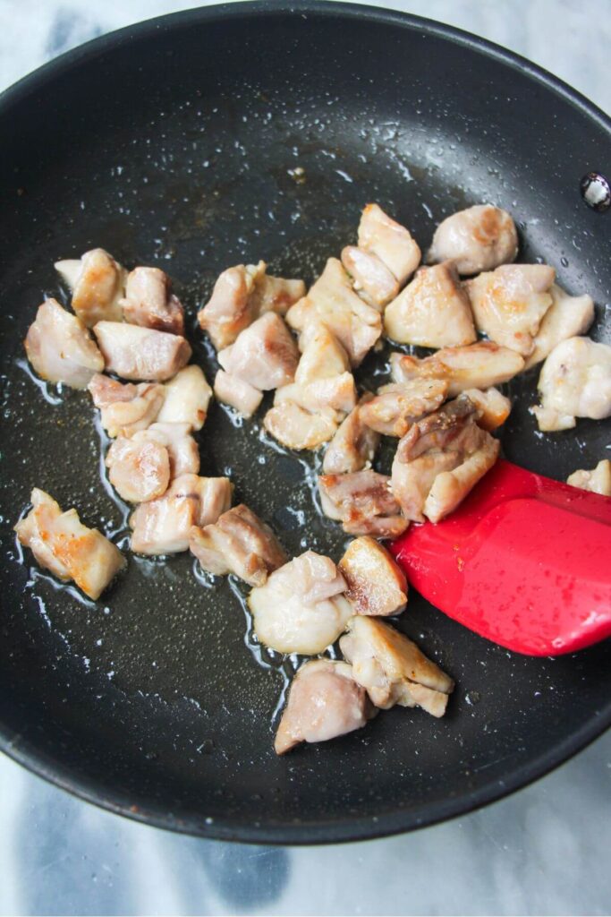 Diced chicken thighs being cooked in a small black pan.