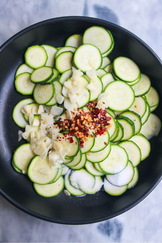 Finely sliced courgette, chilli flakes and sliced garlic in a small black pan.