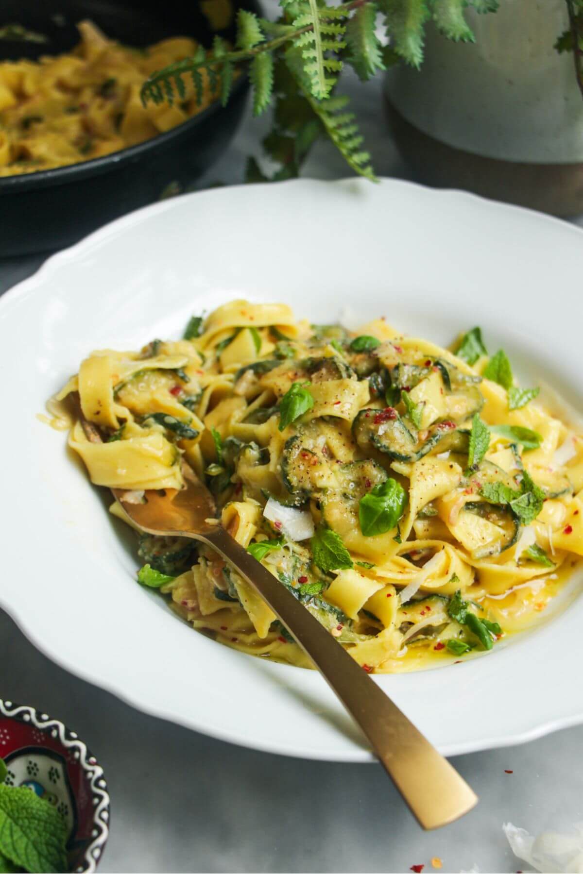 Courgette pasta in a white bowl with a gold fork.