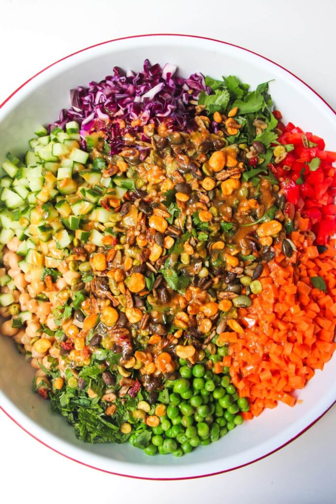 Colourful chopped vegetables in a large white bowl with dressing poured on top.