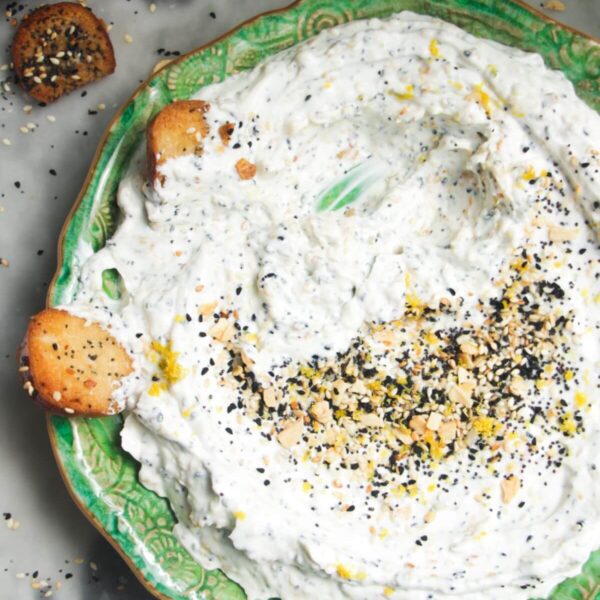 Everything bagel dip on a small green plate with bagel chips on the side.