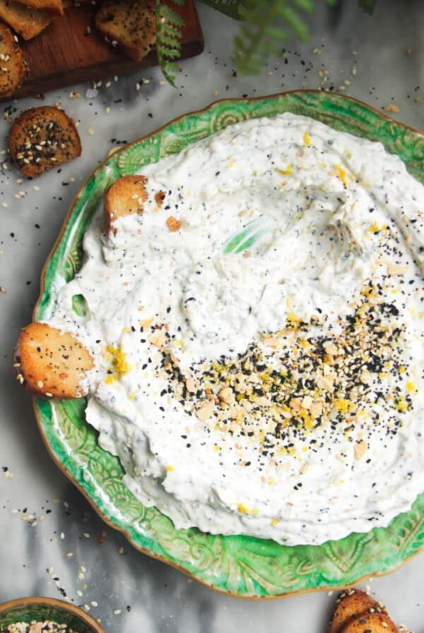 Everything bagel dip on a small green plate with bagel chips on the side.