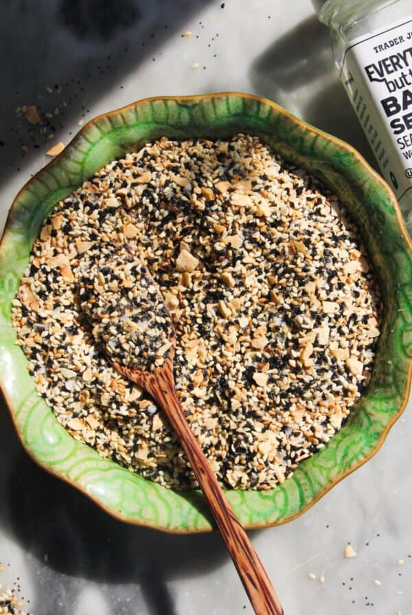Everything bagel seasoning in a green bowl with a wooden spoon inside.