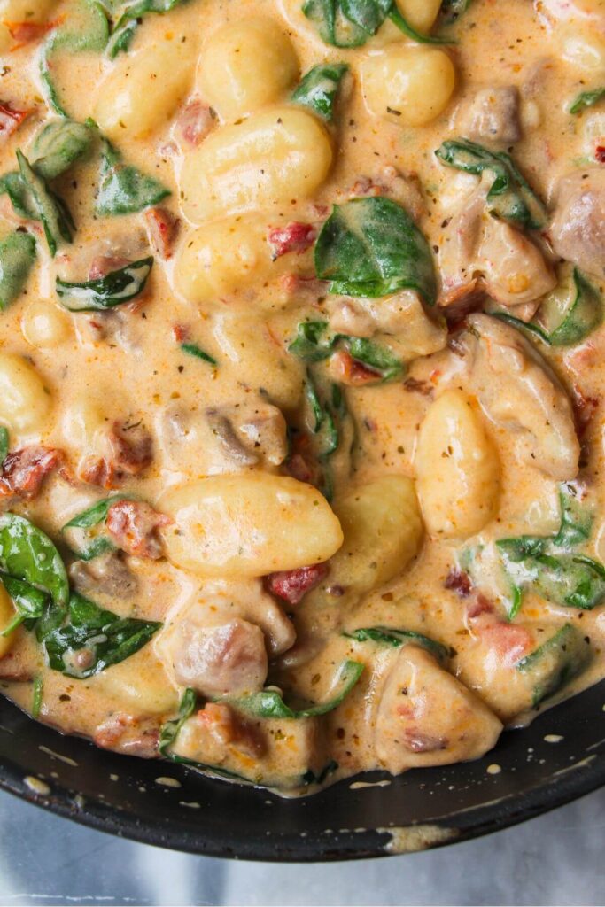Close up of creamy chicken gnocchi in a black pan.