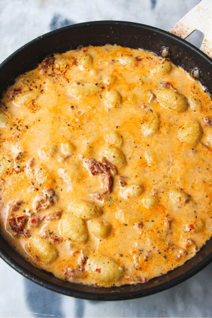 Creamy sundried tomato gnocchi after simmering in a black pan.