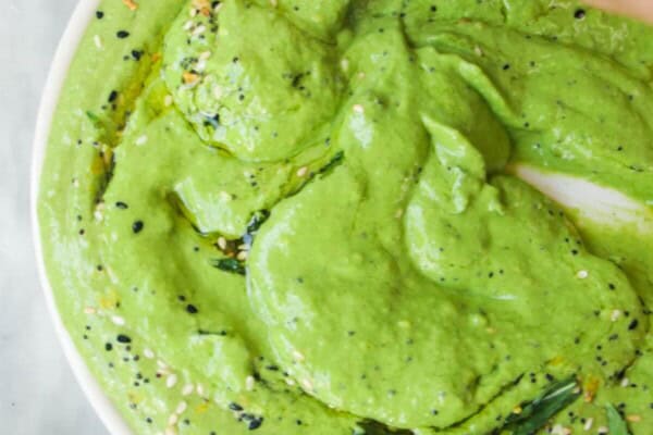 Hand swirling a pita chip through green goddess dip on a white plate.