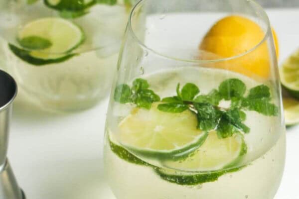 2 glasses of Hugo spritz with lime slices and mint leaves inside.