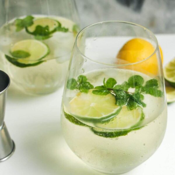 2 glasses of Hugo spritz with lime slices and mint leaves inside.