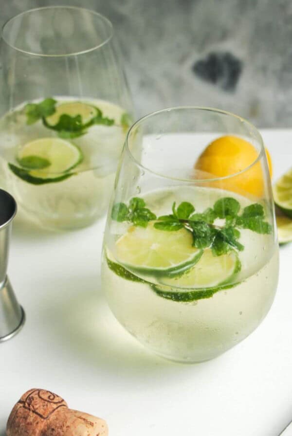 2 glasses of Hugo spritz with lime slices and mint leaves inside.