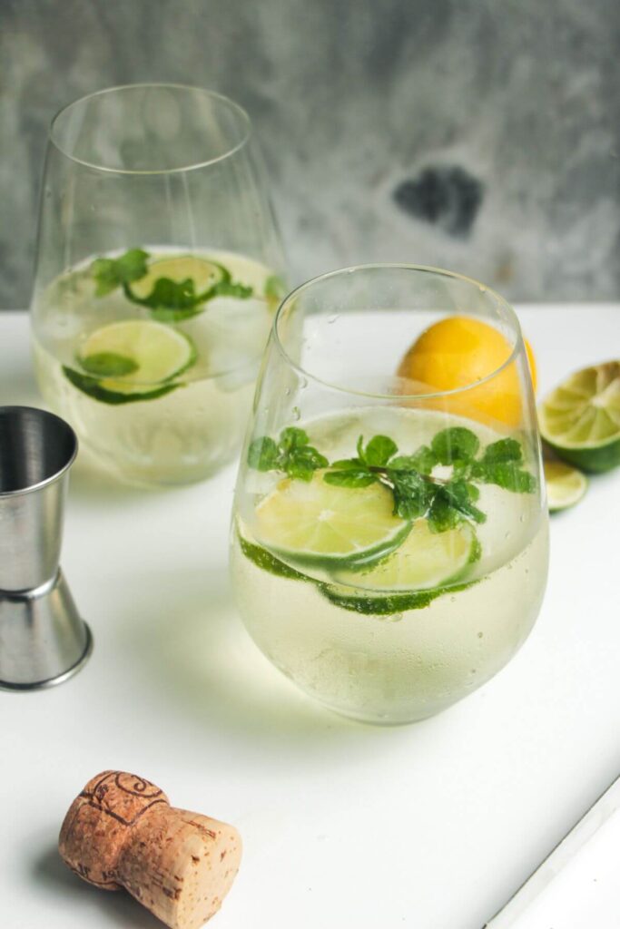 2 glasses of Hugo spritz with lime slices and mint leaves inside.