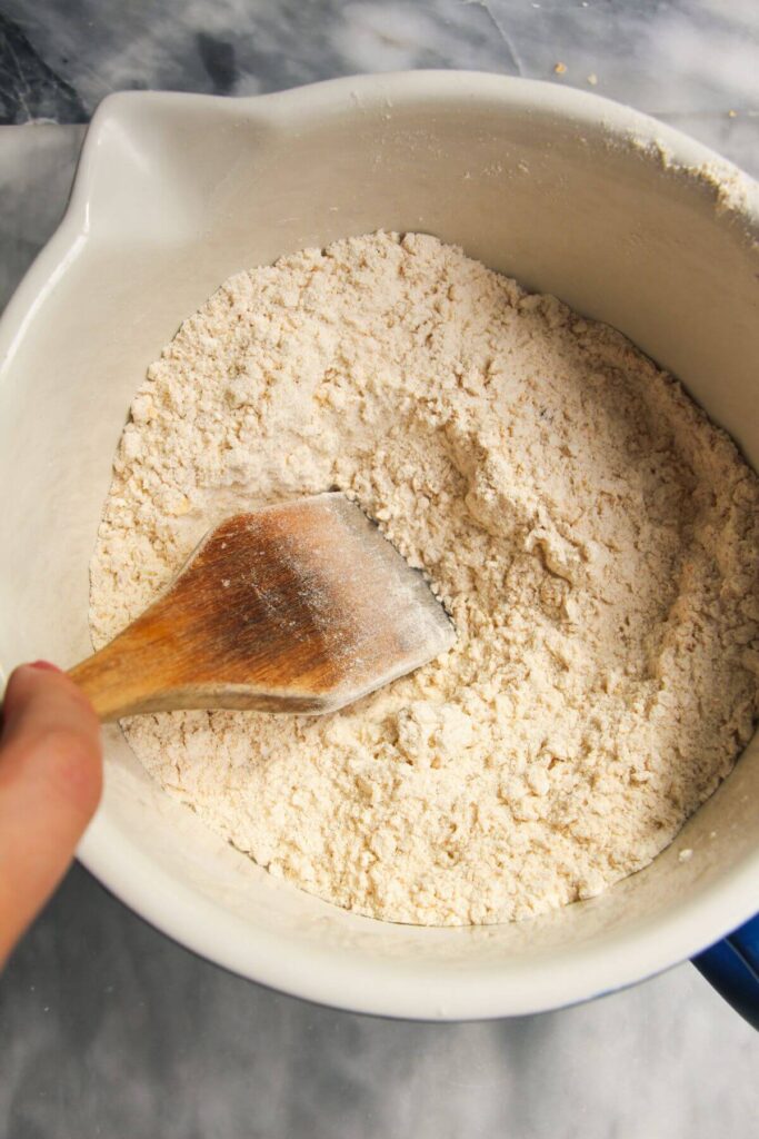 Wooden spatula mixing dry ingredients in a white bowl.