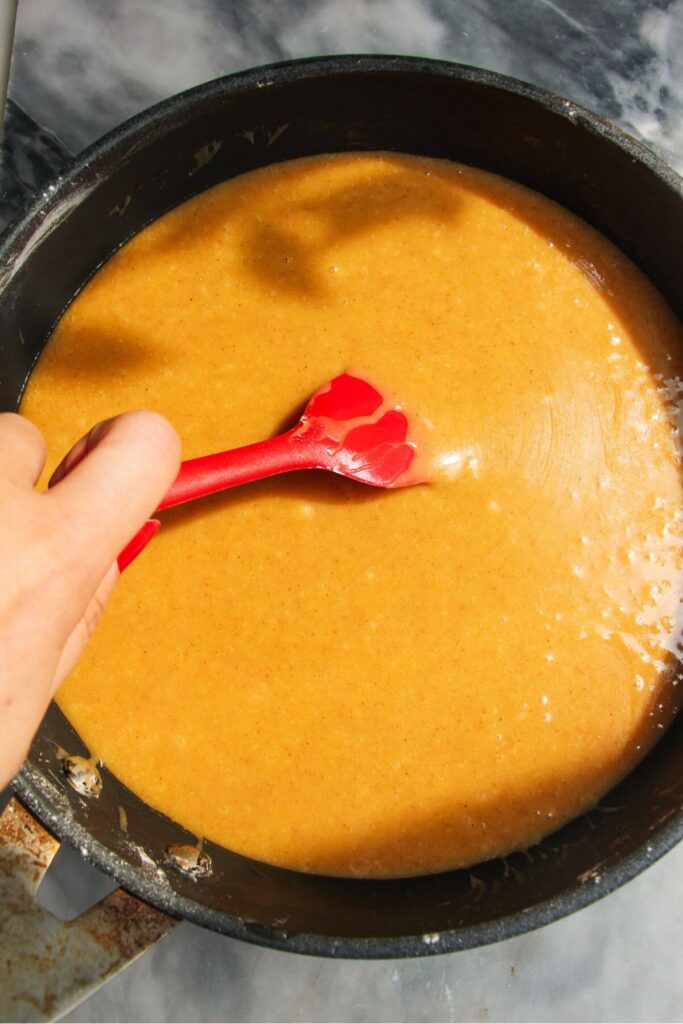 Red spatula mixing ginger icing in a balck pan.