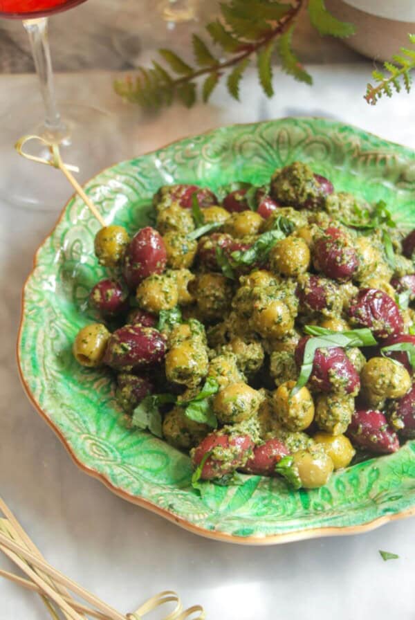 Pesto marinated olives on a small green plate with skewers on the side.