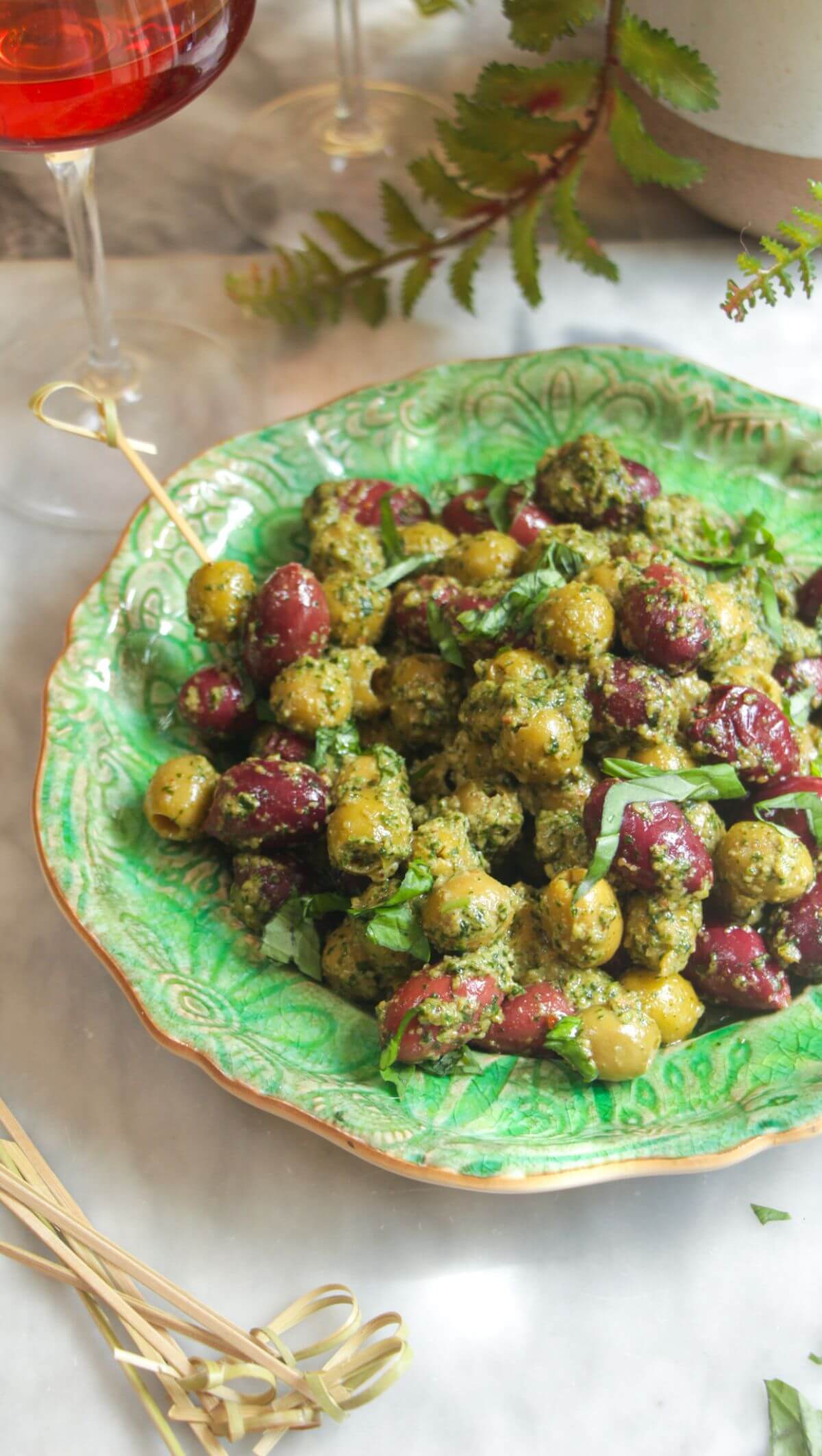 Pesto marinated olives on a small green plate with skewers on the side.