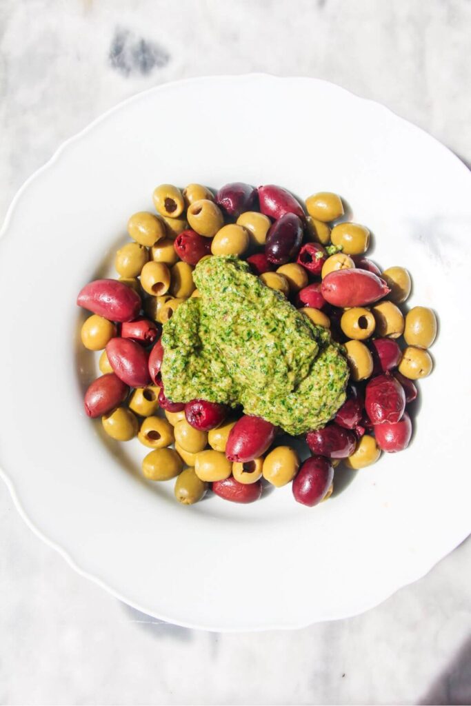 Basil pesto on top of olives in a white bowl.