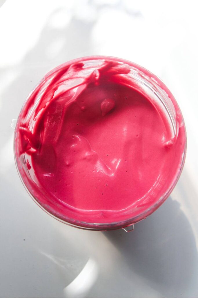 Bright pink beet tahini sauce in a clear cup.
