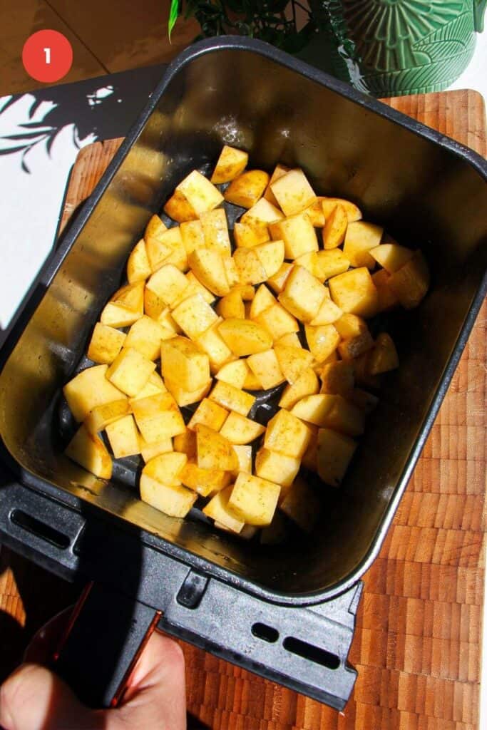 Cubed potatoes tossed in seasoning in air fryer basket.