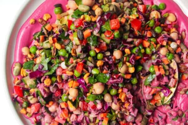 Rainbow chopped salad on pink tahini sauce on a white plate, with extra sauce on the side.