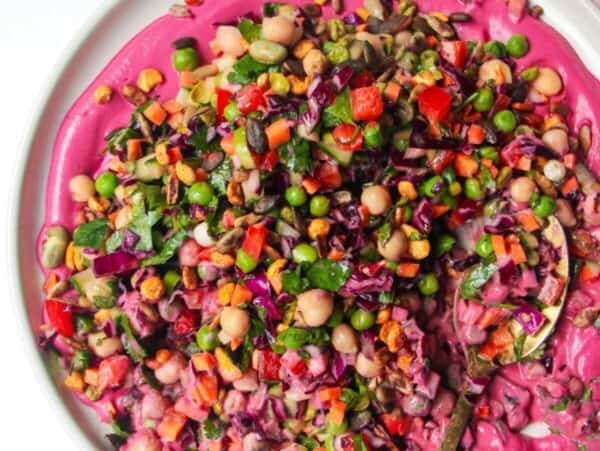 Rainbow chopped salad on pink tahini sauce on a white plate, with extra sauce on the side.