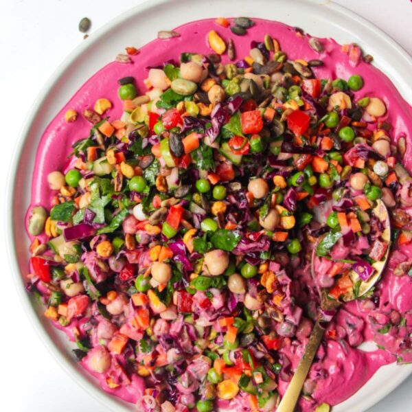 Rainbow chopped salad on pink tahini sauce on a white plate, with extra sauce on the side.