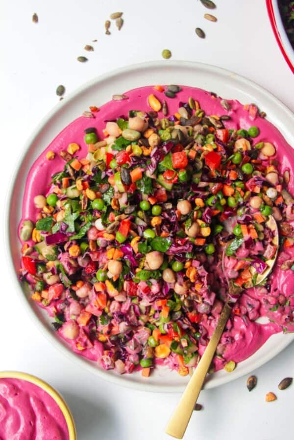 Rainbow chopped salad on pink tahini sauce on a white plate, with extra sauce on the side.