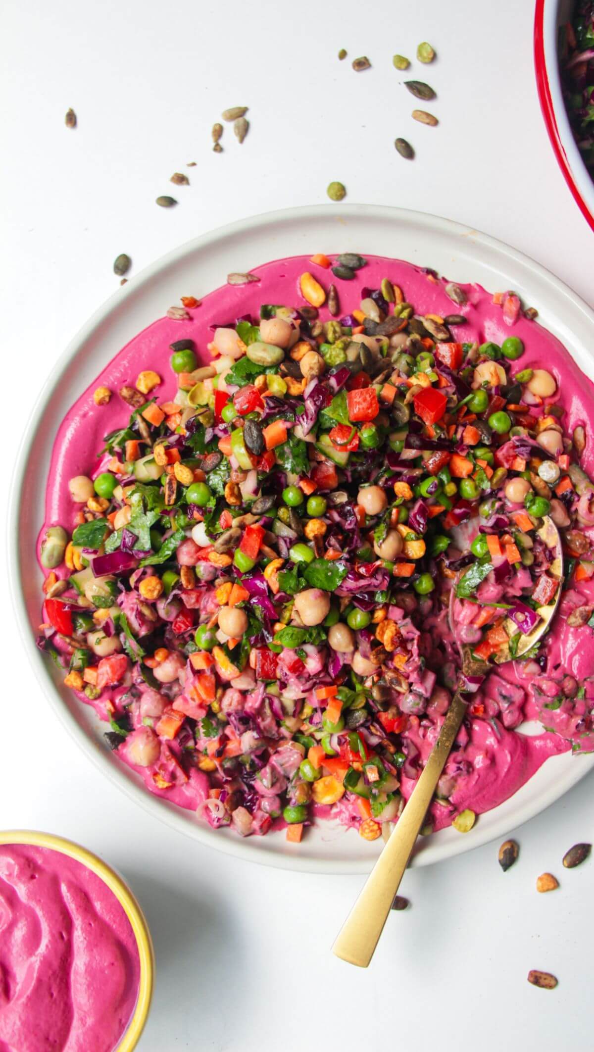 Rainbow chopped salad on pink tahini sauce on a white plate, with extra sauce on the side.