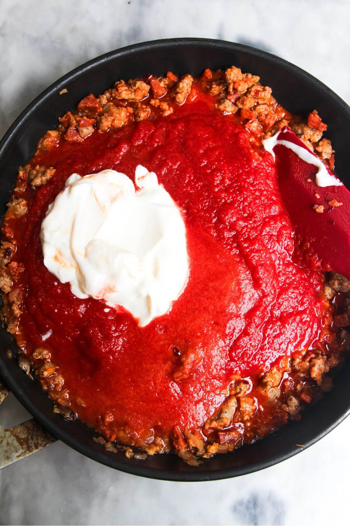 Sour cream and tomato passata added to gnocchi in a pan.
