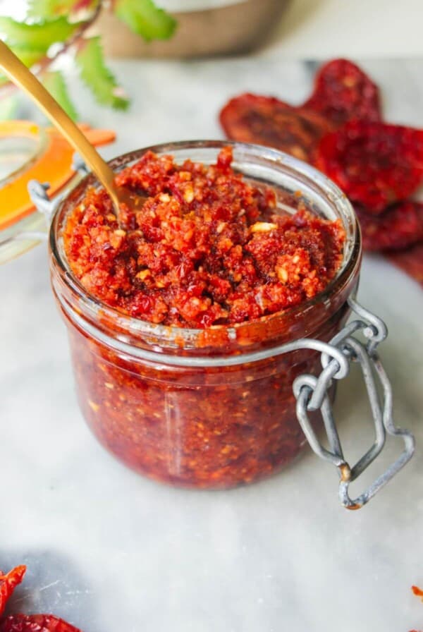 Sun dried tomato pesto in a glass jar with a gold spoon in it.