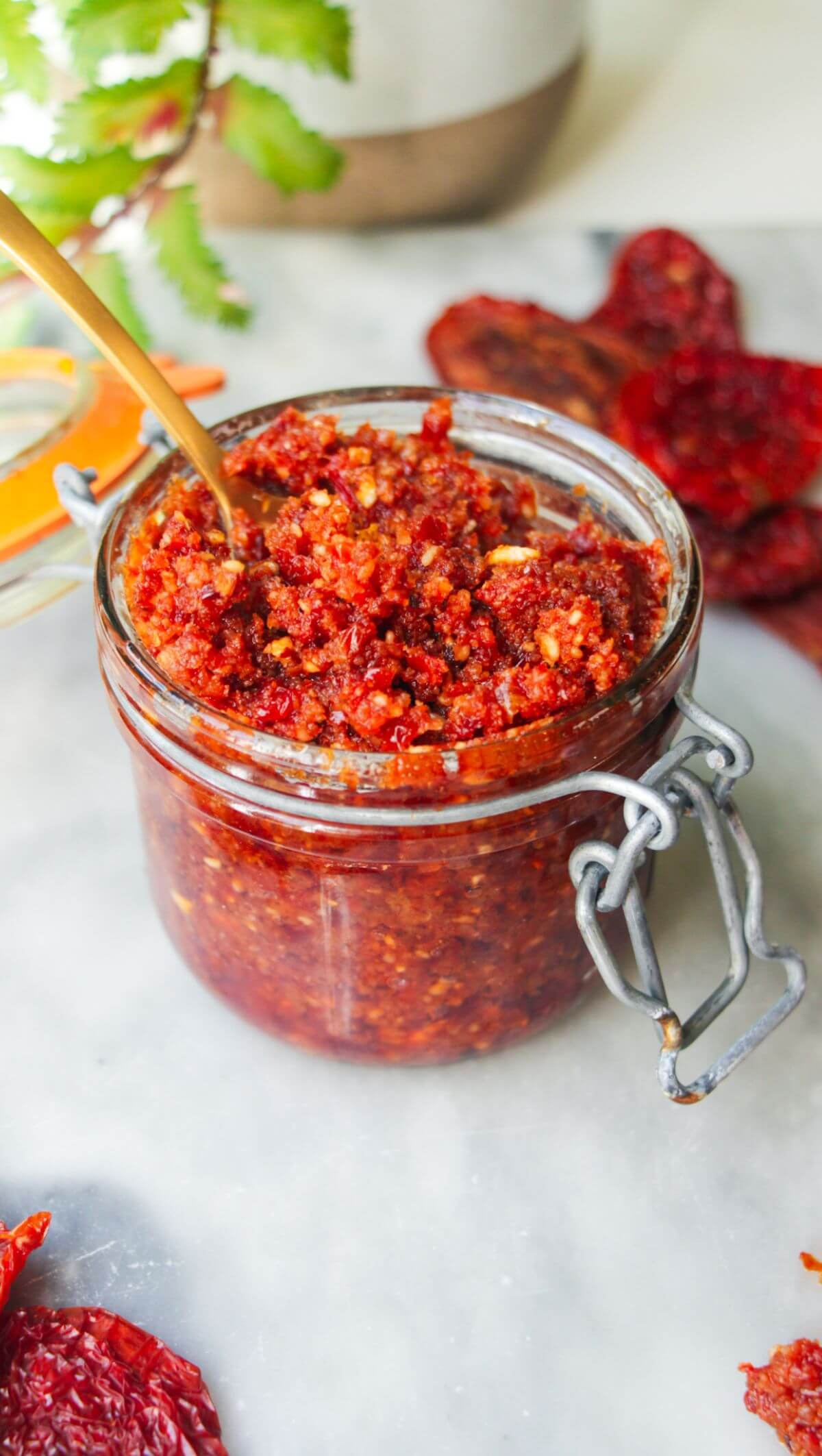 Sun dried tomato pesto in a glass jar with a gold spoon in it.